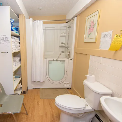 Bathroom with a walk-in bathtub, white curtain, toilet and shelves of towels