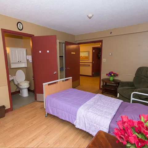 Bedroom with a purple bedcover, green armchair and an open bathroom door