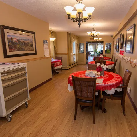 Dining room with round tables, red cloths, wooden chairs and framed landscapes